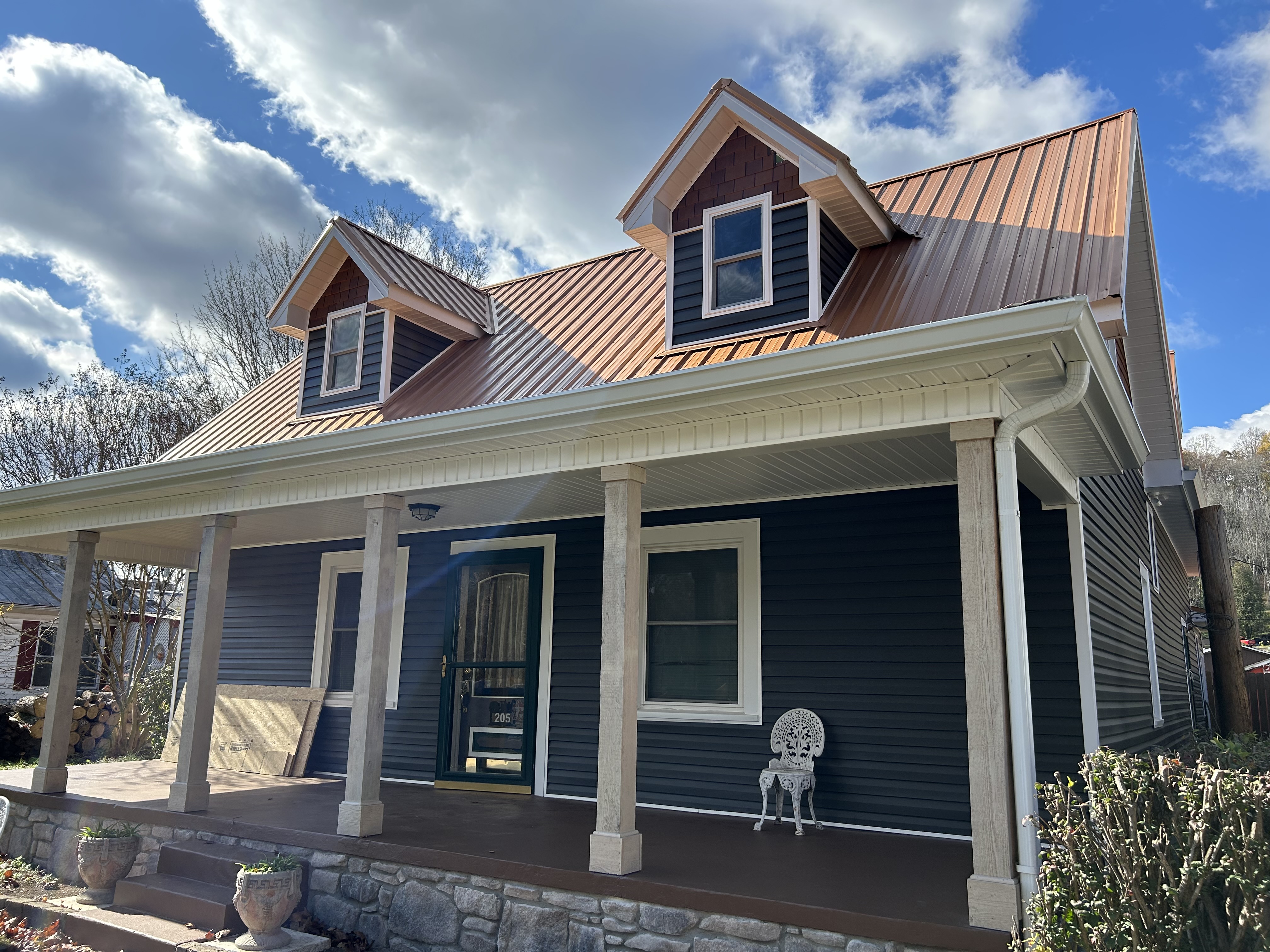 Exterior view of a custom home featuring a metal roof, blue siding, and a porch with columns. A white decorative chair is placed on the porch.
